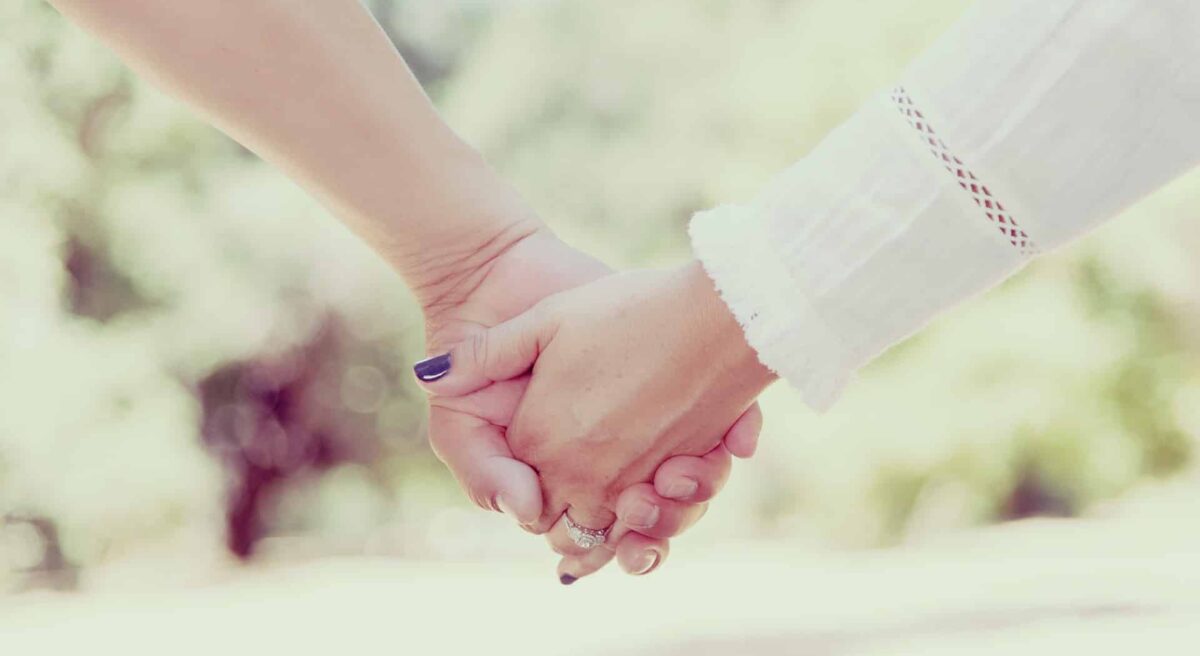 Ein Brautpaar hält Händchen. Erfahren Sie mehr über die Bedeutung des Gelübdes 'Bis der Tod uns scheidet' und alternative Formulierungen für Ihre Trauung.